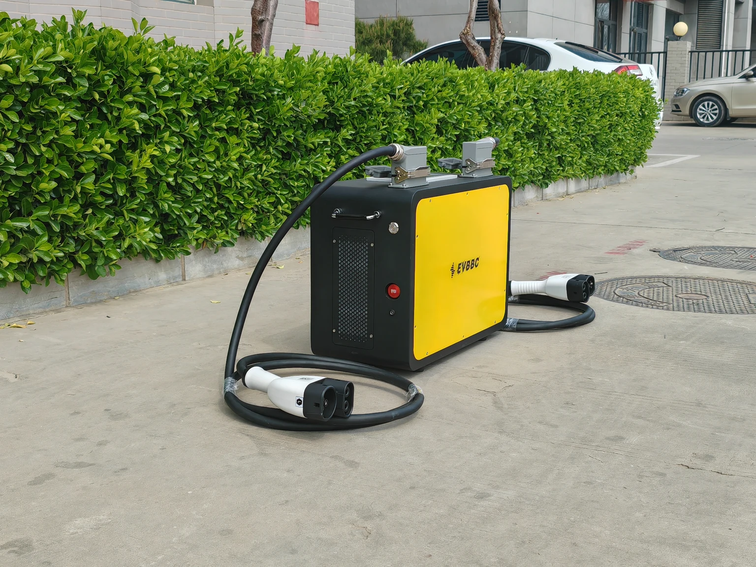 Side-angle photograph of the EVBBC portable V2V charger showing its cooling vent, emergency stop and two cables